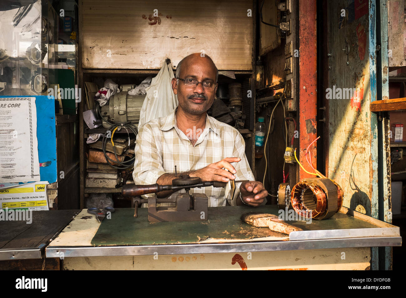 A man sits behind the counter in his shop repairing small electrical