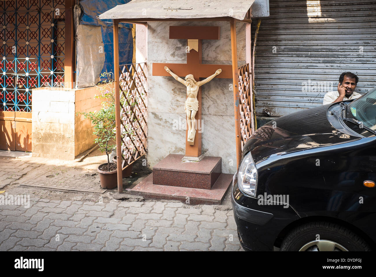 A man talks on his mobile phone outside a shuttered shop next to a small shrine to Jesus Christ. Stock Photo