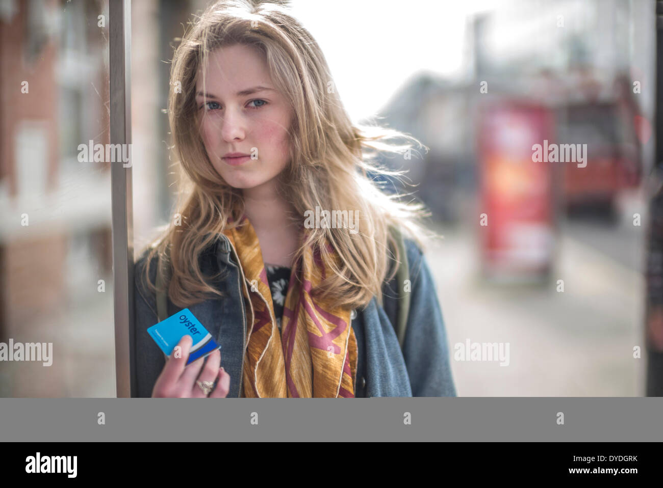 A young woman holds an Oyster card at a London bus stop. Stock Photo