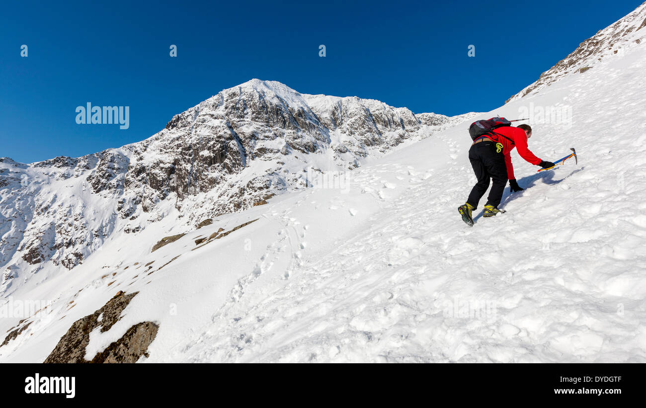 Tourist climbs the snowy Miners Track over Glaslyn in the Snowdonia National Park. Stock Photo