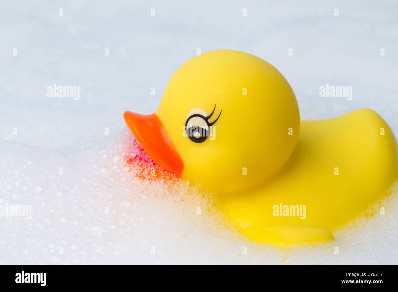 A yellow plastic duck floating in a frothy bubble bath Stock Photo