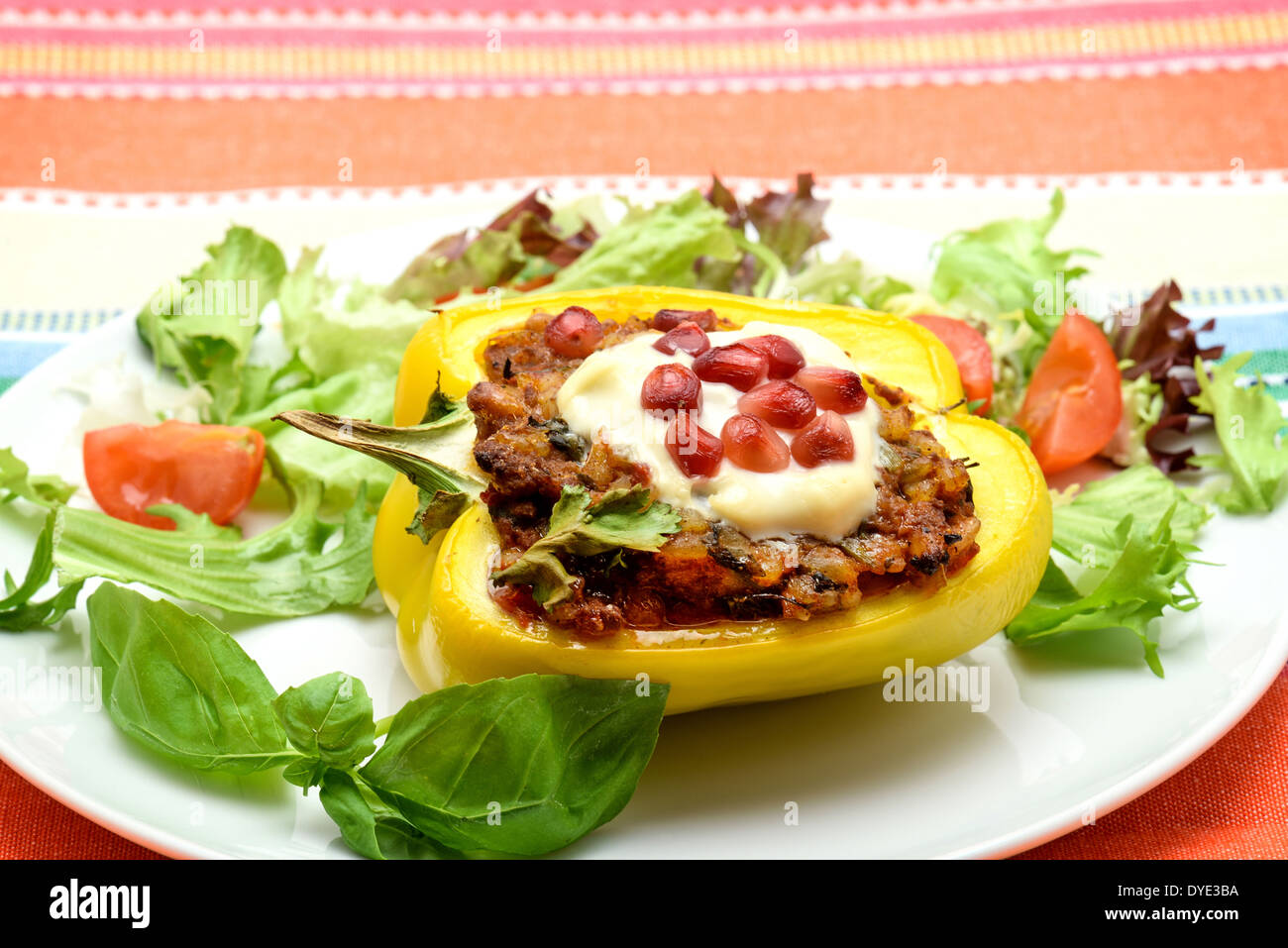 A yellow bell pepper with a savoury stuffing that has been roasted in an oven then served on a white plate with a side salad Stock Photo