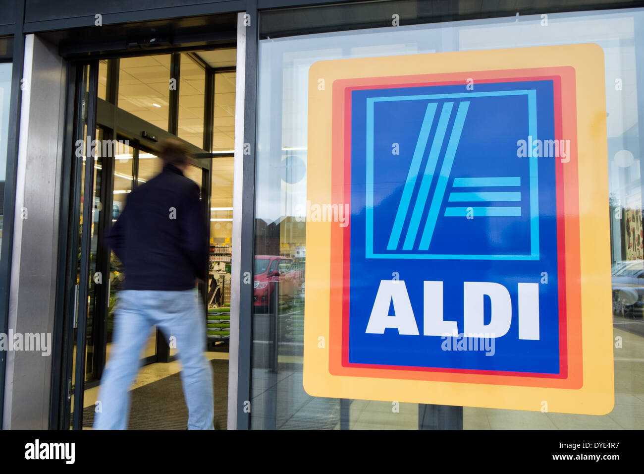 A man, motion blurred, walking into a branch of Aldi supermarket to shop. Showing the sign & identity of the store Stock Photo