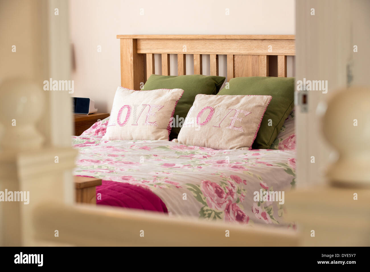 A lifestyle image of a bed in a homely bedroom with pillows with the word love embroidered upon them & a rose print bed cover Stock Photo