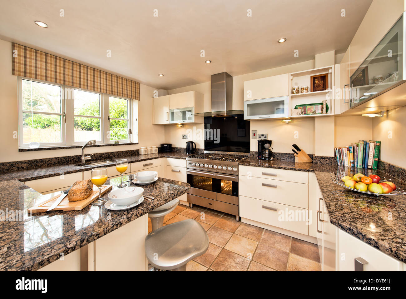 The interior of a modern fitted domestic kitchen with range, cabinets & granite work surfaces Stock Photo
