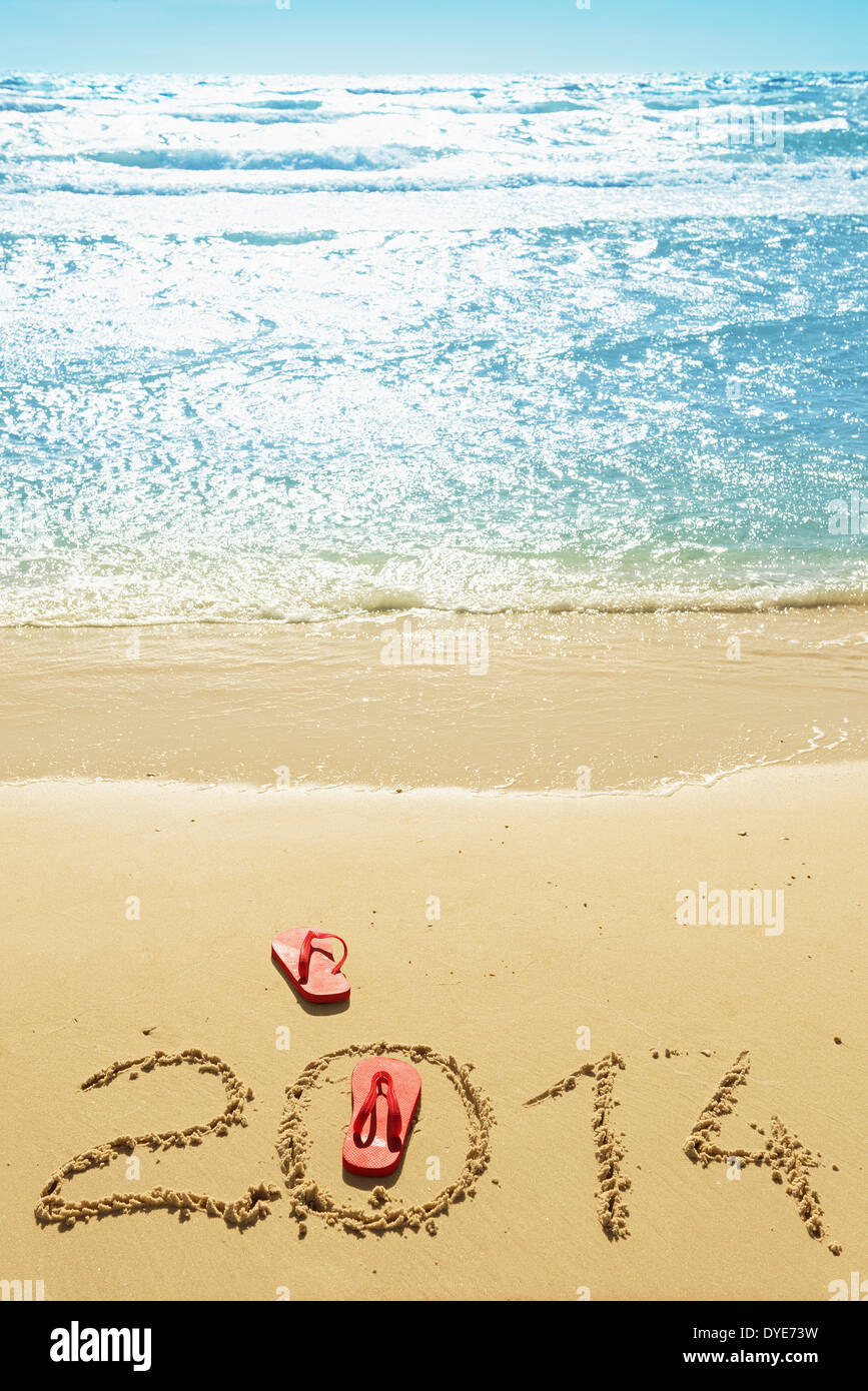 Red flip flops and digits 2014 on the beach sand.Concept of summer vacations and new year Stock Photo