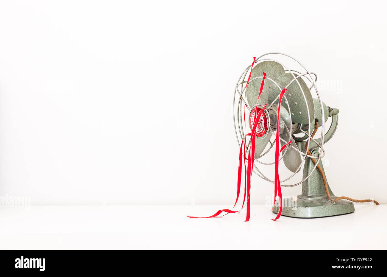 An old green desk fan with red ribbons against a white background Stock