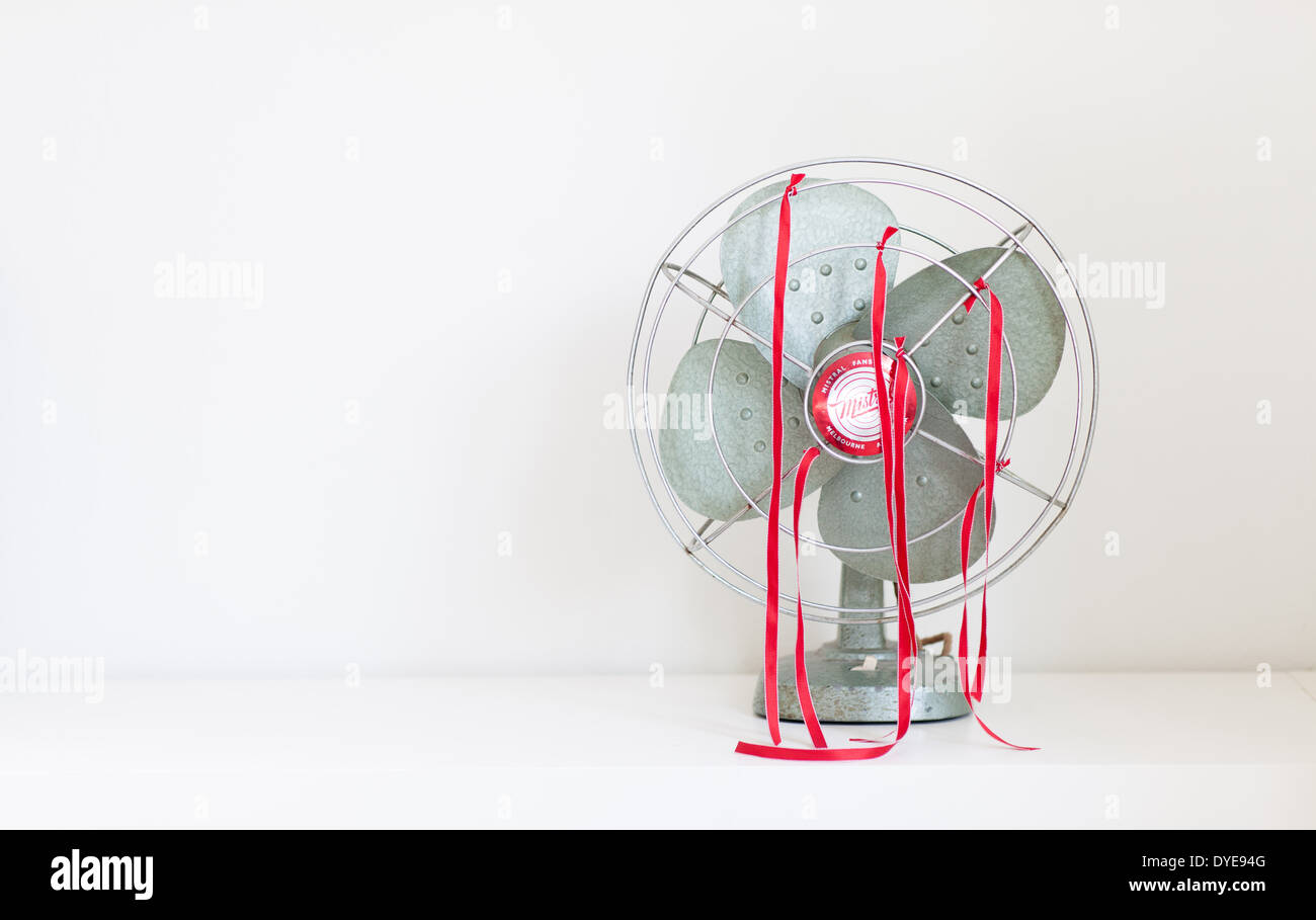 An old green desk fan with red ribbons against a white background Stock