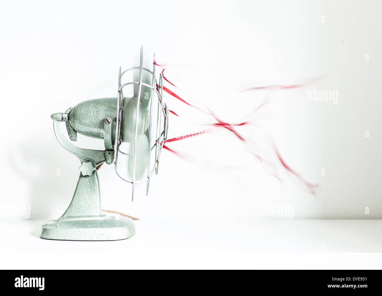 An old green desk fan with red ribbons against a white background Stock