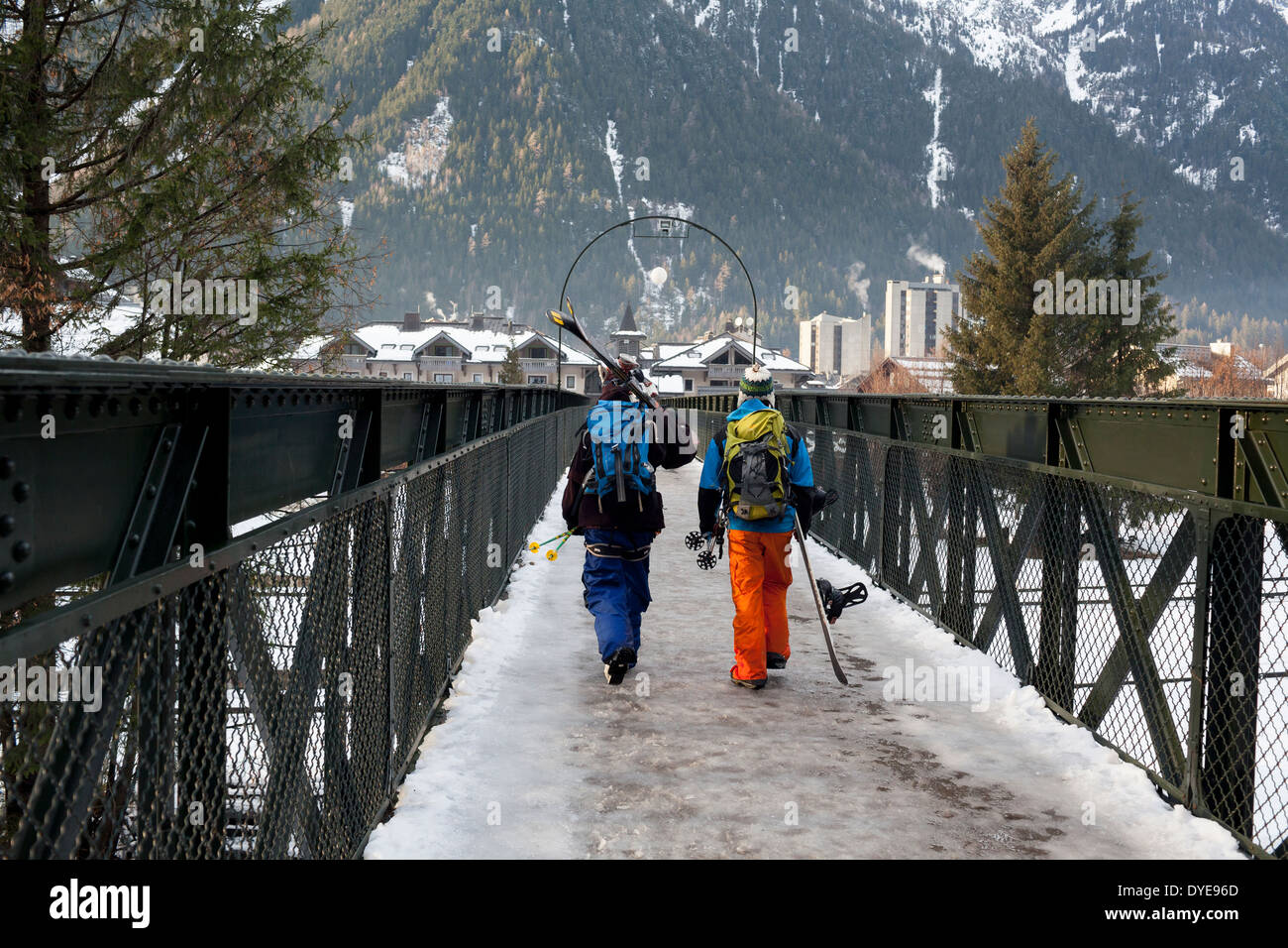 A skier and snowboarder cross a pedestrian bridge in the village of Chamonix Mont-Blanc. Stock Photo