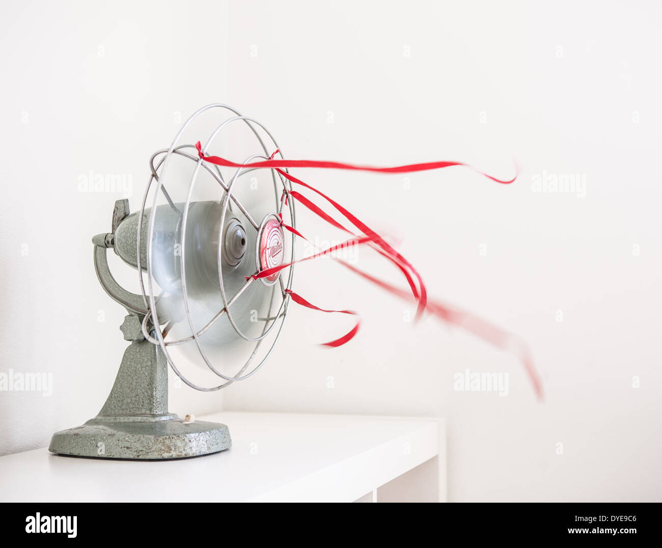 An Old Green Desk Fan With Red Ribbons Against A White Background