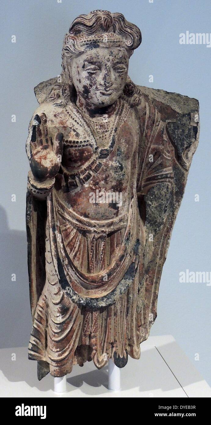 The bodhisattva Maitreya, Pakistan, Gandhara, 3rd century painted and gilded slate. Maitreya, the Buddha of the future, is making the abhaya mudra, or 'fear not' gesture. His webbed fingers are a sign of his divine nature. This figure shows that Buddhist art in Gandhara, which was in contact via trade routes with religions around the Mediterranean Sea, was influenced by Greco-Roman sculpture. The drapery folds of the Maitreya's lower garment, for instance, recall Roman figures, while his hairstyle is based on representations of the Greek god Apollo. Stock Photo