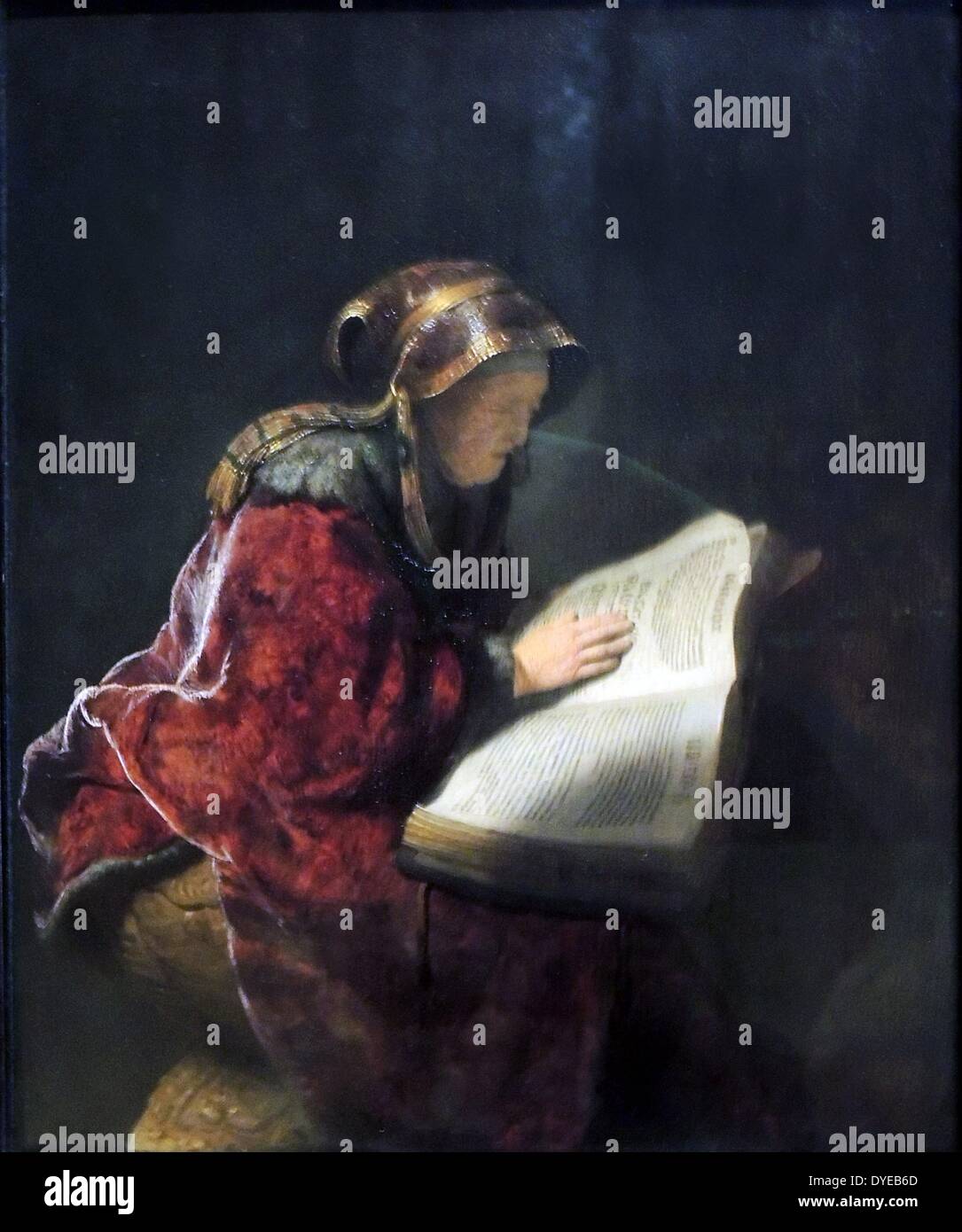 An Old Woman Reading, Probably the Prophetess Hannah by Rembrandt Harmens van Rijn (1606-1669) oil on panel, 1631. Light comes in from behind the old woman: the vivid glow illuminates the book and her hand, so thickly painted that the wrinkles seem almost modelled in clay. Her face remains in shadow. The woman could be the biblical prophetess Hannah. According to the Gospel of Luke, she was an elderly widow who worshipped God night and day with fasting and prayer. Stock Photo