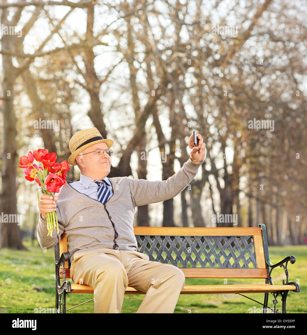 Senior holding flowers and taking selfie in park Stock Photo