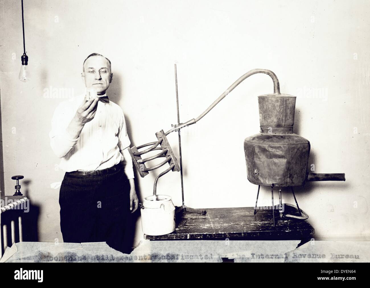 Moonshine still recently confiscated by the Internal Revenue Bureau photographed at the Treasury Department between 1921 and 1932. Man standing next to still looking at contents of glass. Stock Photo
