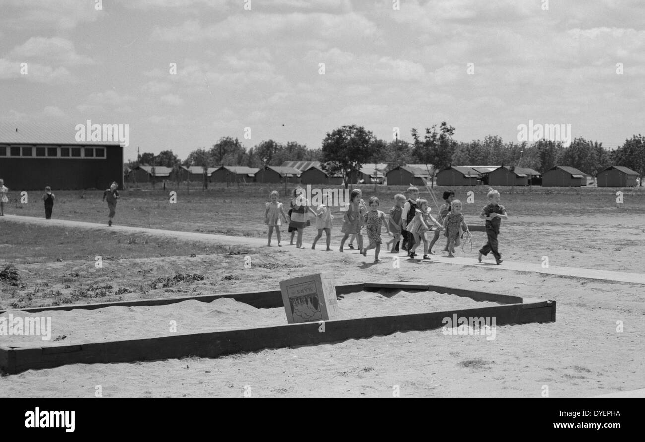 Tulare County, California. Farm Security Administration (FSA) camp for migrant agricultural workers. Nursery school children. Row of prefabricated steel shelters in which their families live shown in background by Dorothea Lange 1895-1965, dated 19380101 Stock Photo