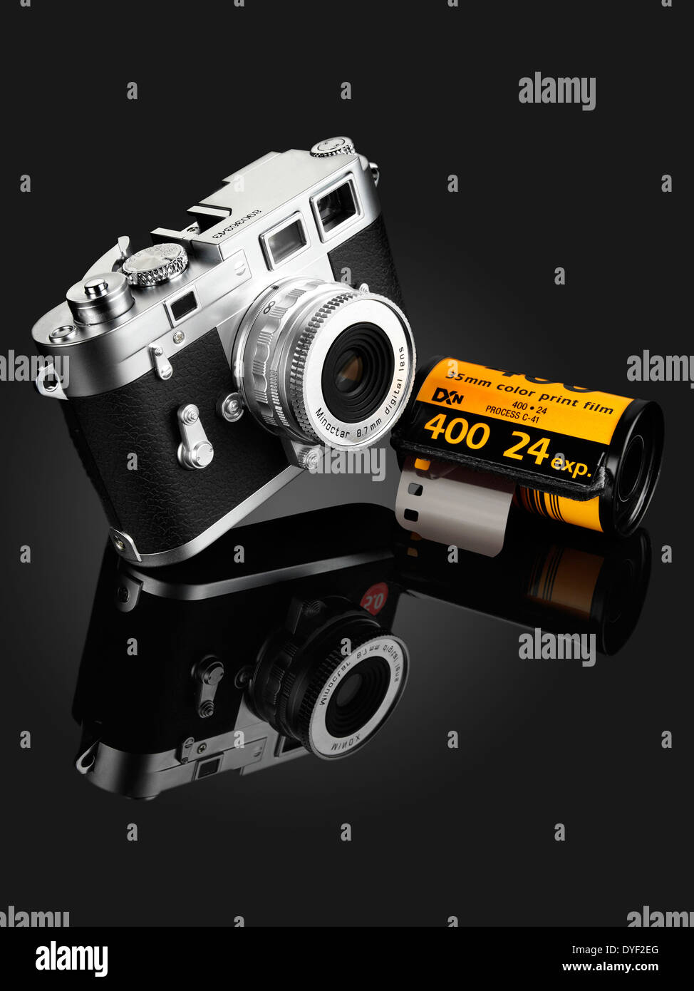 A FUJIFILM SILVER AND BLACK CAMERA WITH A ROLL OF KODAK FILM ON A GRADUATED BLACK BACKGROUND WITH REFLECTION Stock Photo