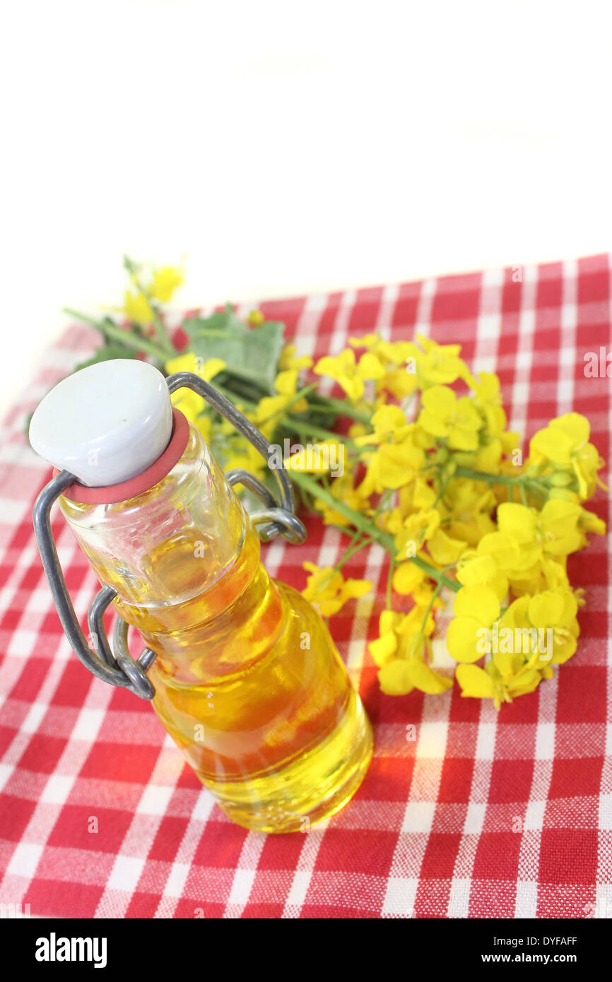 a bottle of rapeseed oil and rapeseed flowers against white background Stock Photo