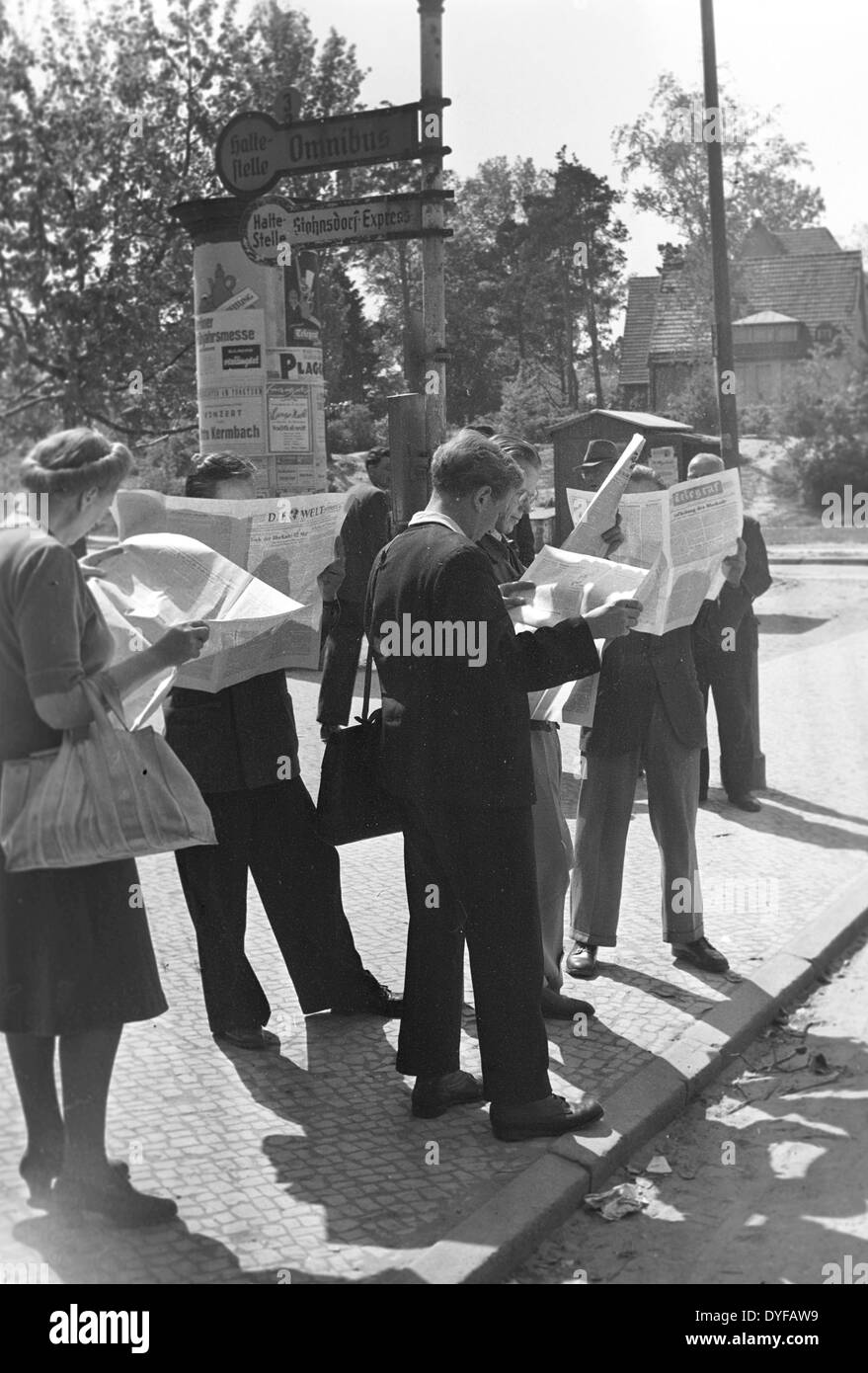 The end of the Berlin Blockade - Berlin citizens are reading about the announced lifting of the Berlin Blockade in the daily news, at a bus station of 'Stahnsdorf Express' in Berlin. Stock Photo
