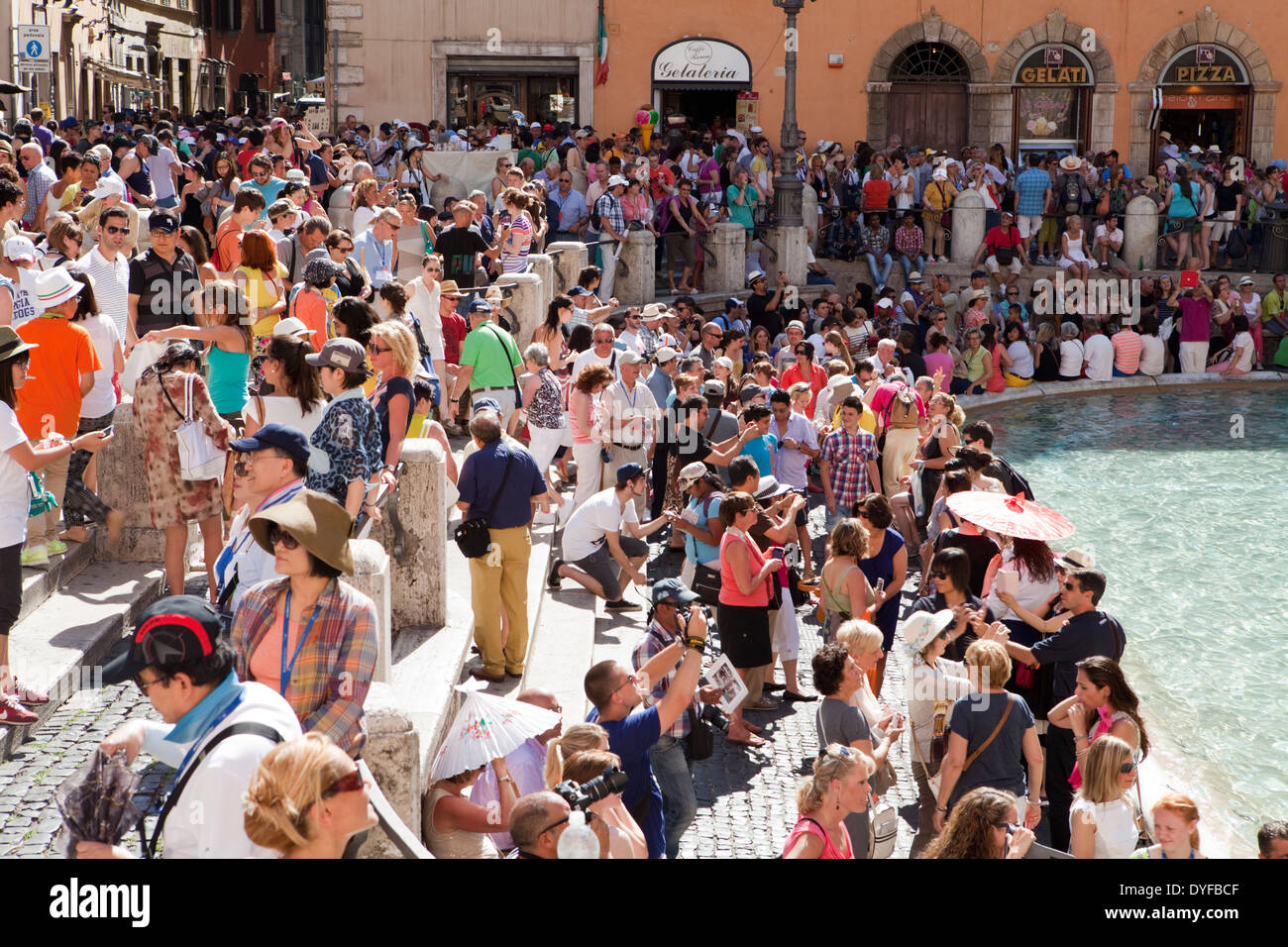 Crowds of tourists throw coins and take selfies at the edge of the Trevi Fountain in Rome Stock Photo