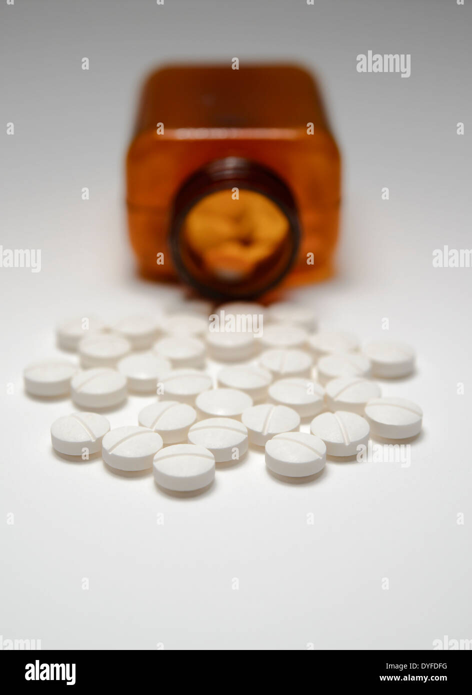 Generic white pills on a white background, spilled from a brown plastic medicine bottle. Stock Photo