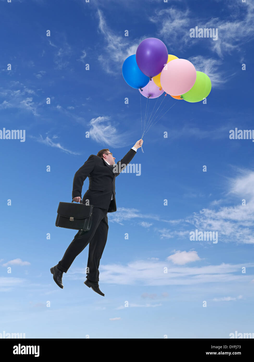 Businessman wearing black suit holding suitcase flying in the air being raised by bunch of colorful balloons Stock Photo
