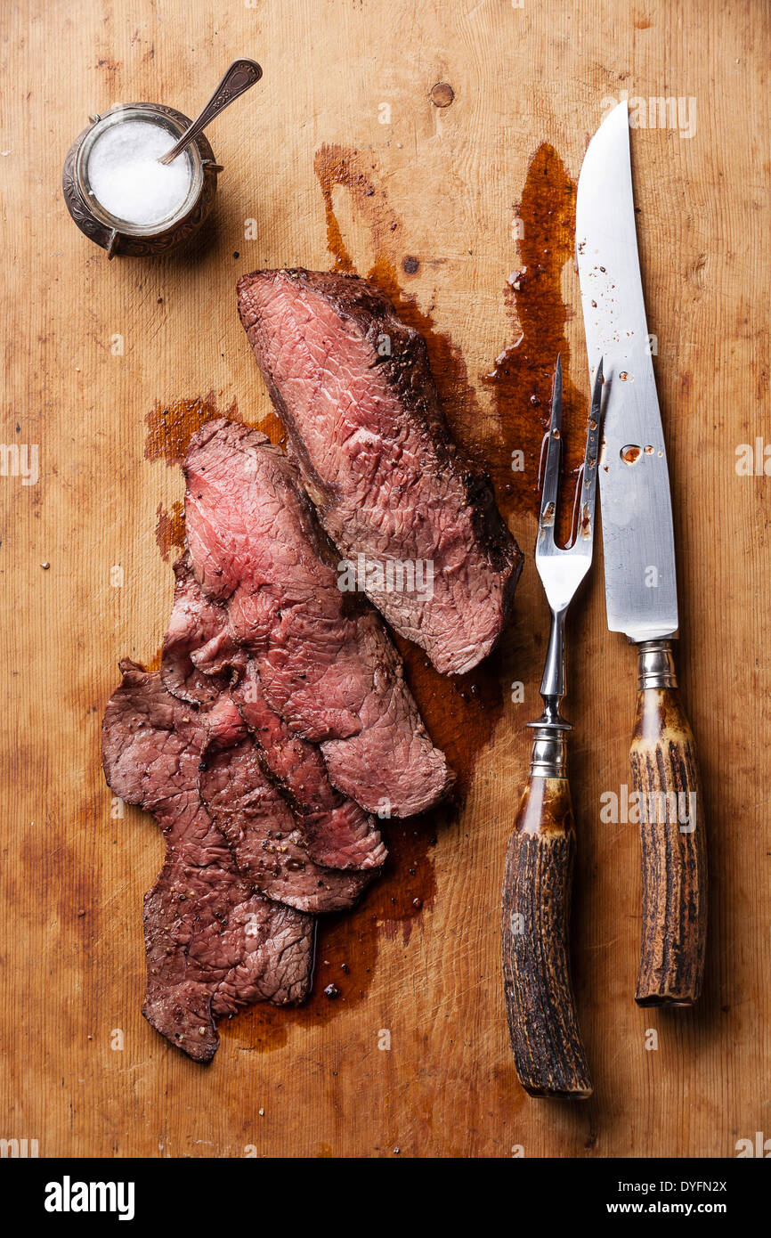 Roast beef with knife and fork for meat on wooden background Stock Photo