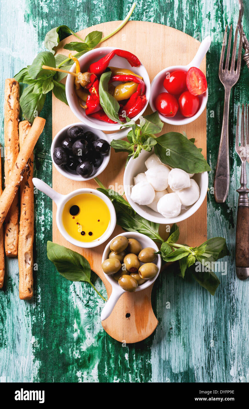 Mixed antipasti olives and mozzarella served on wooden cutting board over green wooden table with vintage fork. Top view. Stock Photo