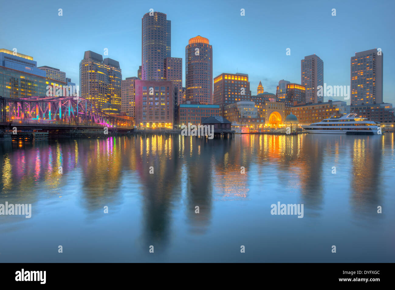 The skyline is illuminated and reflected off the waters of the harbor as twilight descends on Boston, Massachusetts. Stock Photo
