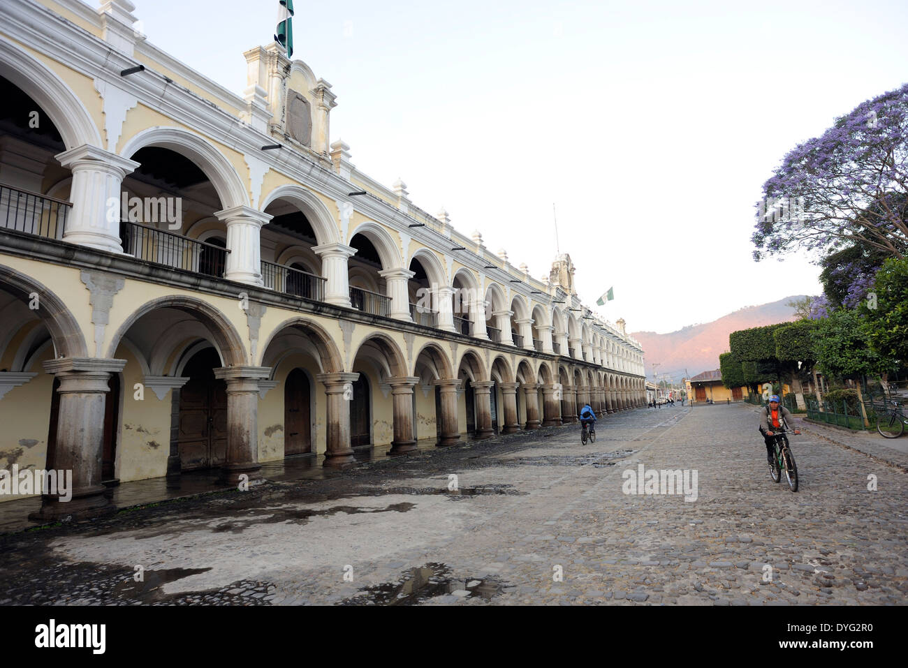 Early morning commuters cycle over the cobbles of 3 Calle in front of  of  El Ayuntamiento, the town hall, building. Stock Photo