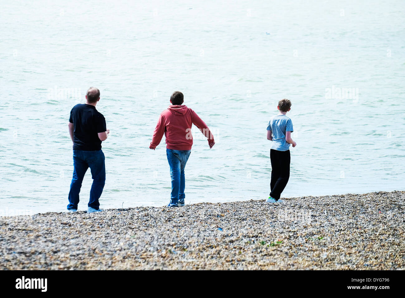 A father and his two sons throwing pebbles into the sea at Southend in Essex in the UK. Stock Photo
