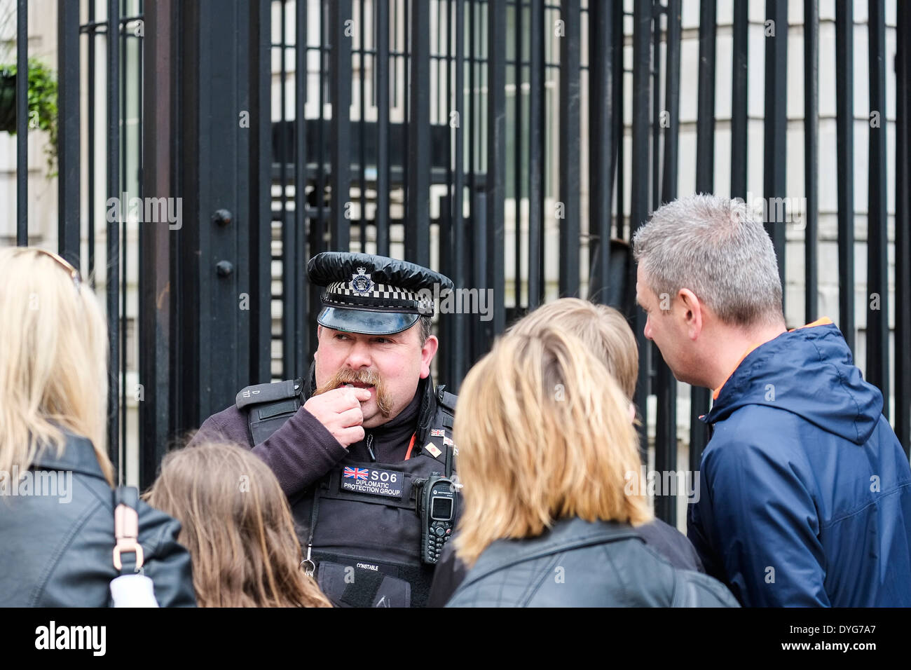 Tourists talk to a police officer from the Diplomatic Protection Group on duty outside the gates of Downing Street in London. Stock Photo