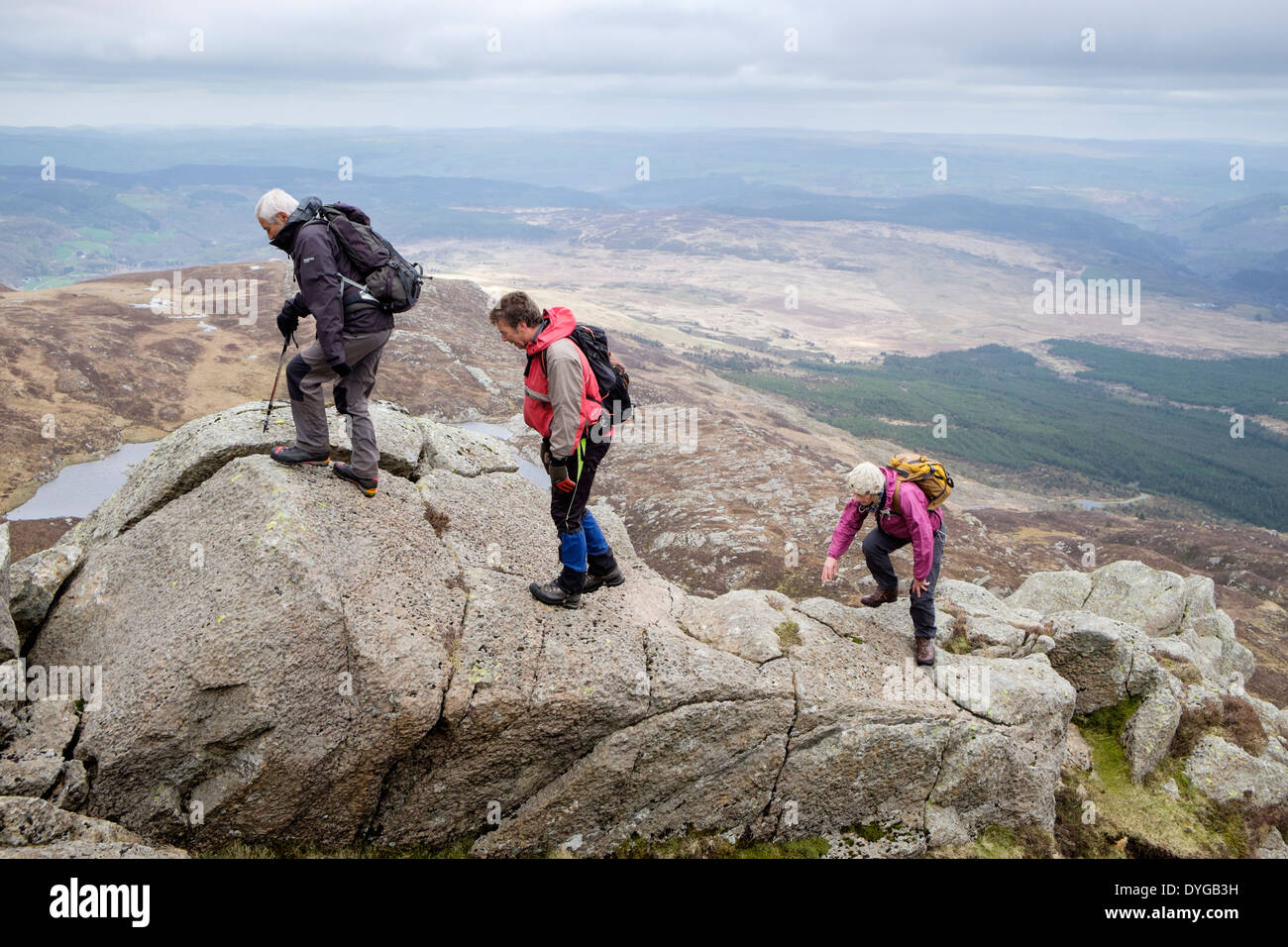 Three hikers scrambling up hill over rocks on Carnedd Moel Siabod Daear Ddu east ridge in mountains of Snowdonia National Park Wales UK Stock Photo