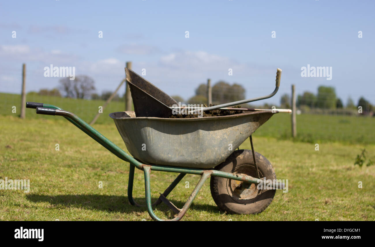 old and worn wheel barrow resting on  grass containing horse manure Stock Photo