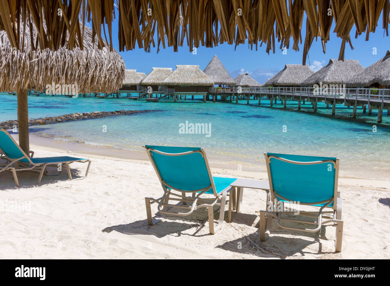 Lounge chairs on beach by thatched roof hut overlooking overwater bungalows in French Polynesia Stock Photo