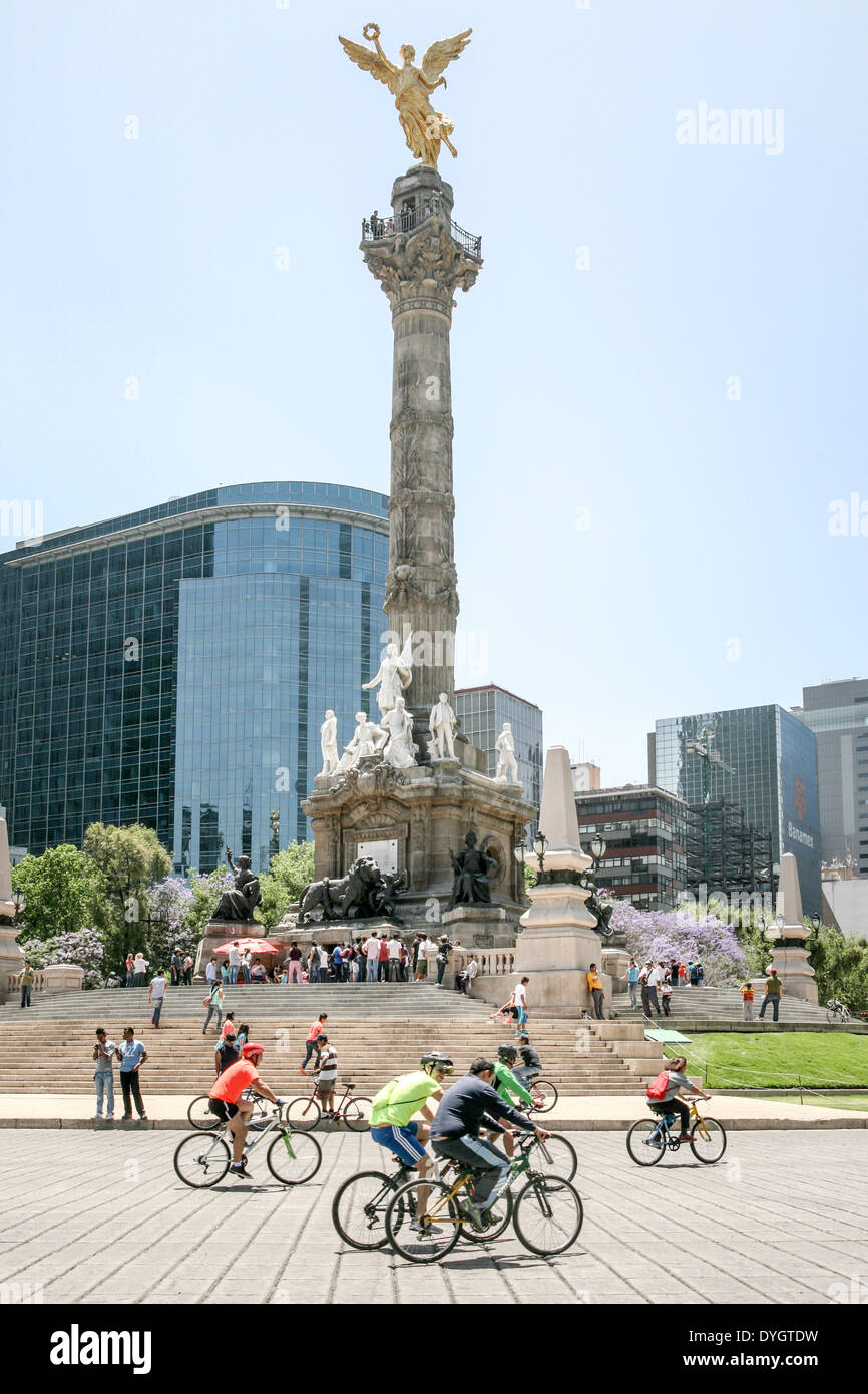 bicyclists enjoy traffic free Paseo de la Reforma  glorieta roundabout below crowd on steps waiting to enter Angel monument Stock Photo