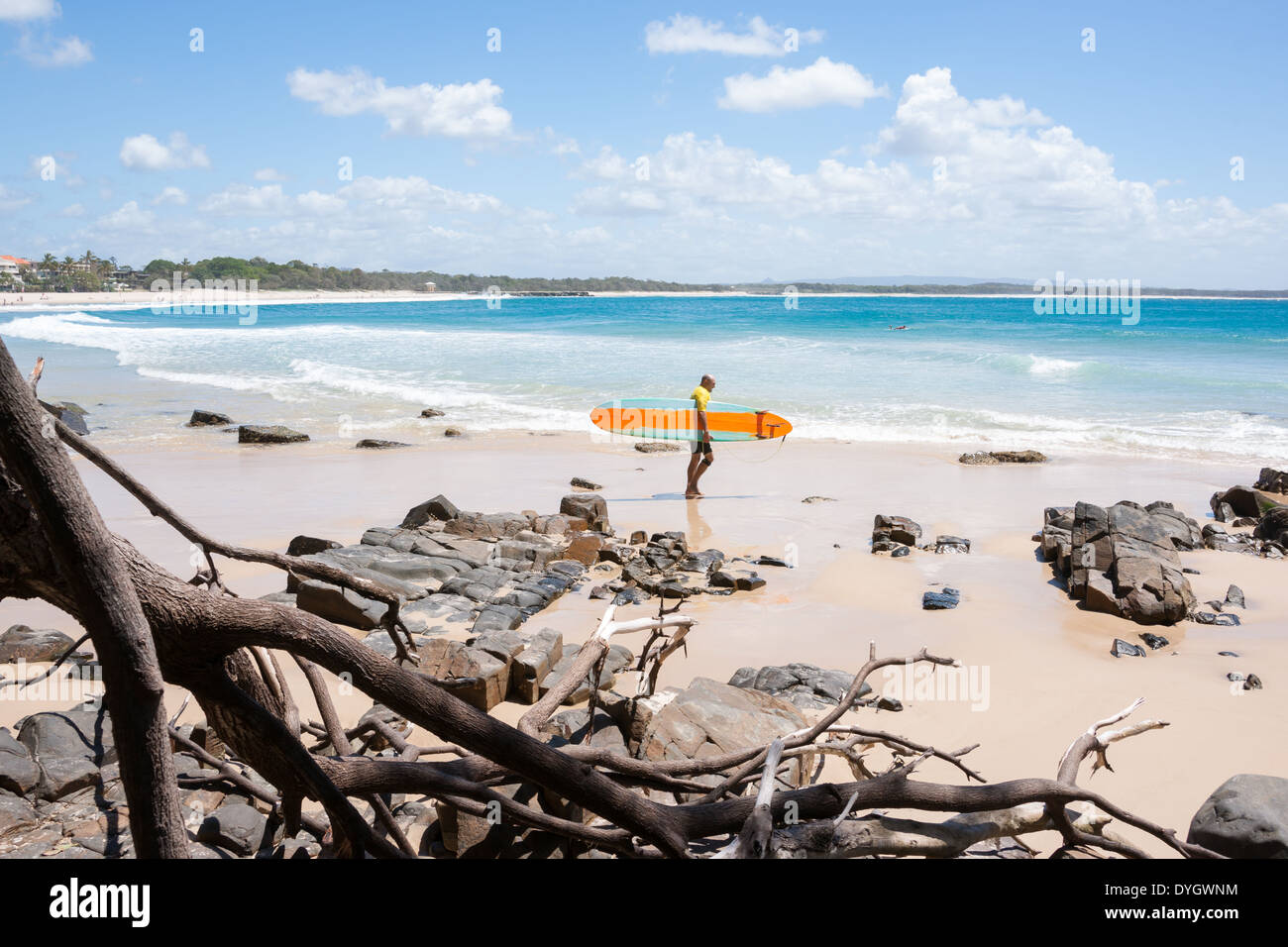 Surfer carries his yellow longboard surfboard towards the surf at the