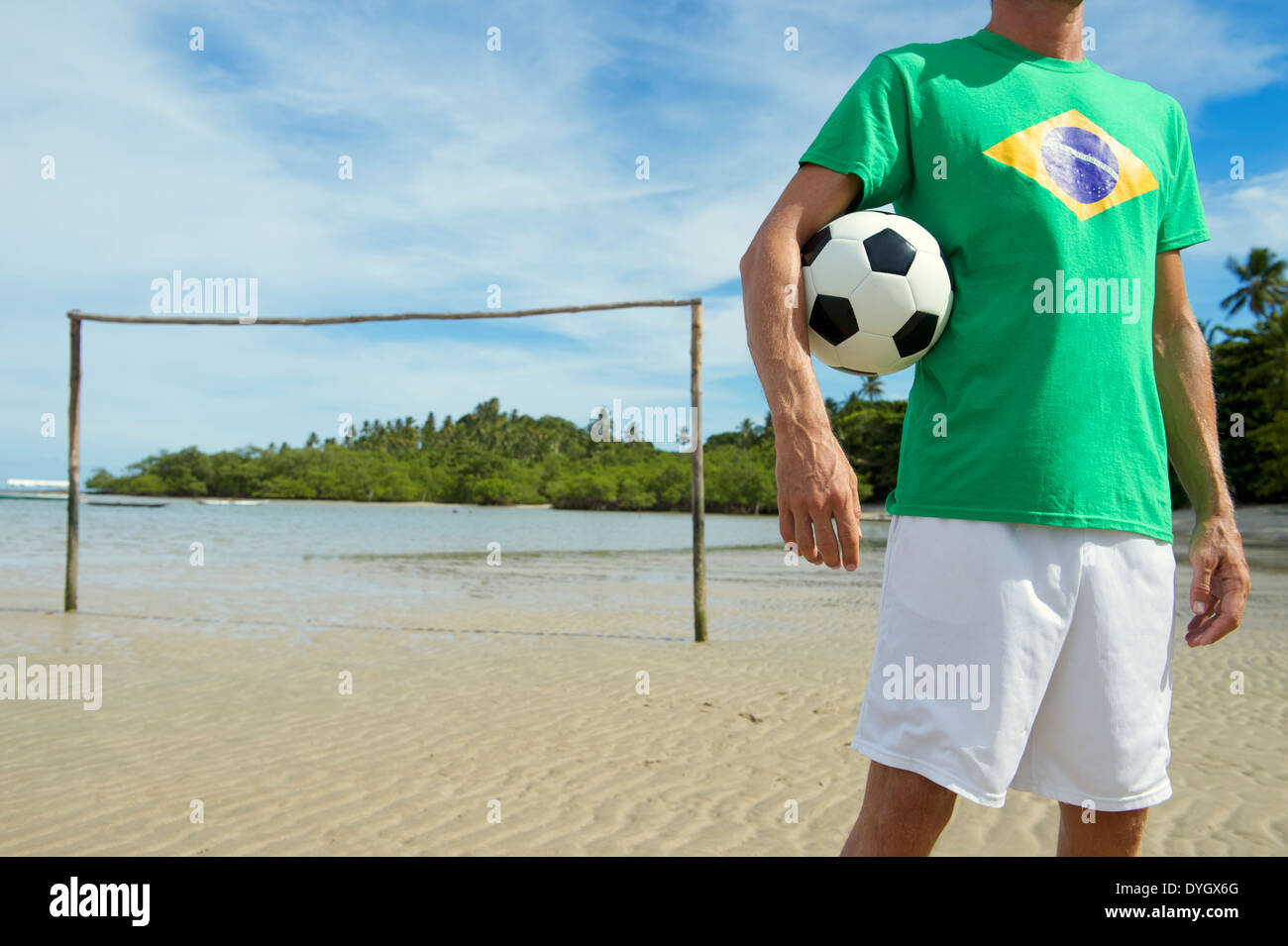 Football player holding soccer ball sitting on simple Brazilian beach