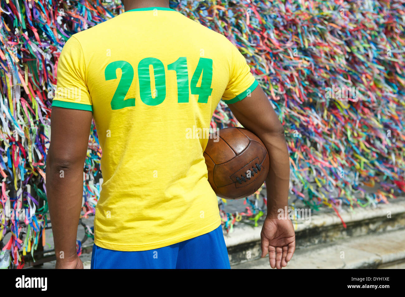 Brazil 2014 soccer player standing with vintage brown football in front of wall of colorful lembranca wish ribbons in Salvador Stock Photo