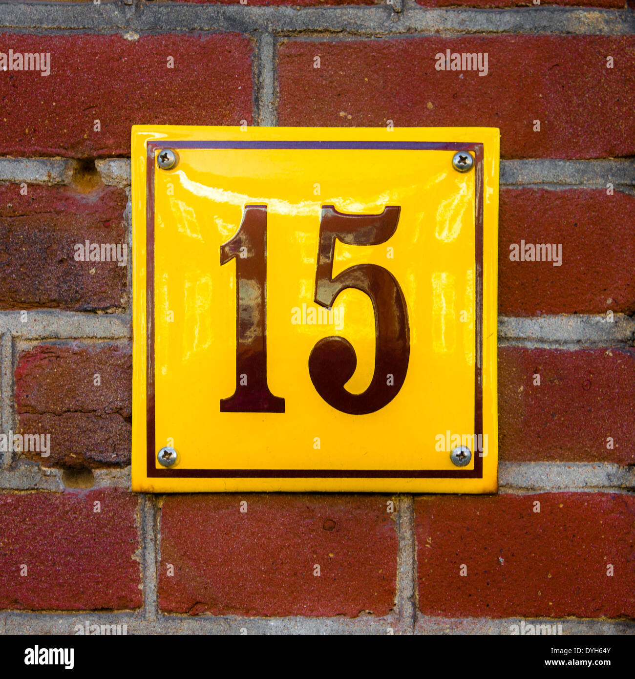 Enameled house number fifteen. Brown lettering on a yellow background. Stock Photo