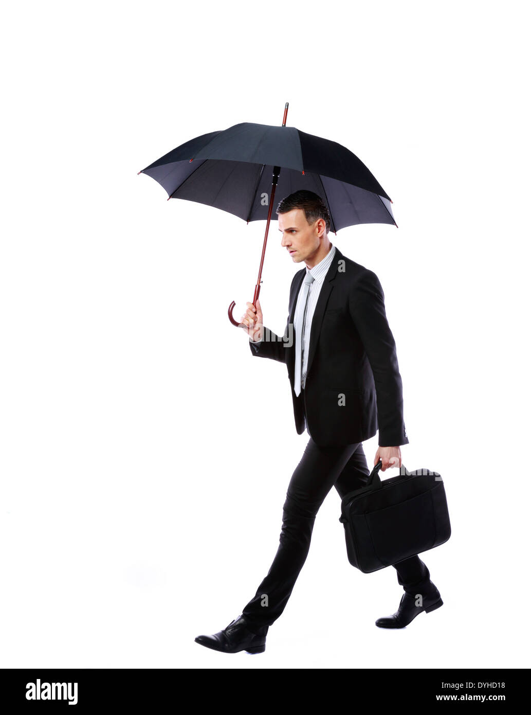 Businessman walking with umbrella and laptop bag on gray background Stock Photo