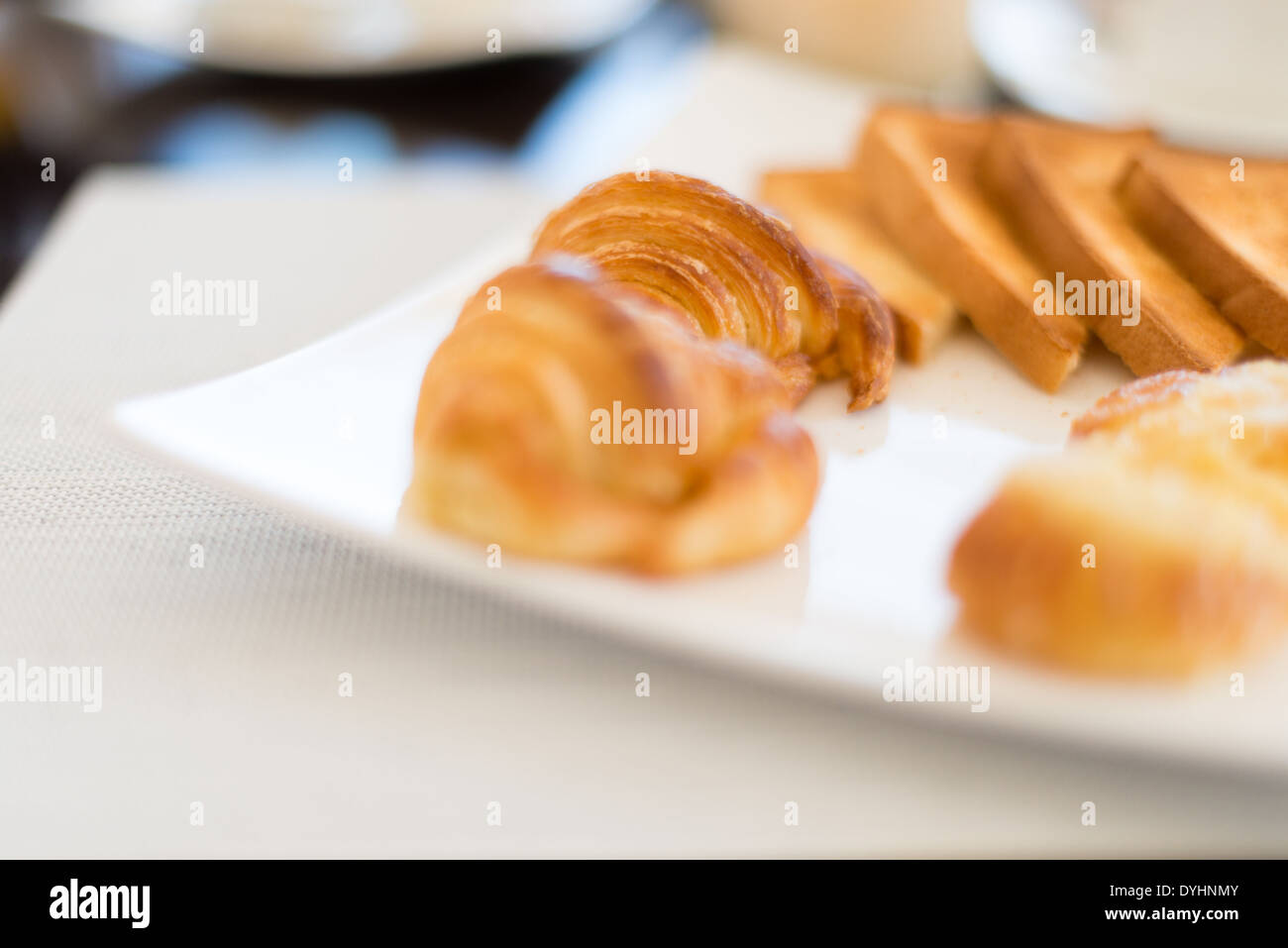 Close-up view of tasty croissants and toasts on square plate served on table with white mat. Fresh appetizing pastry with crisp. Stock Photo