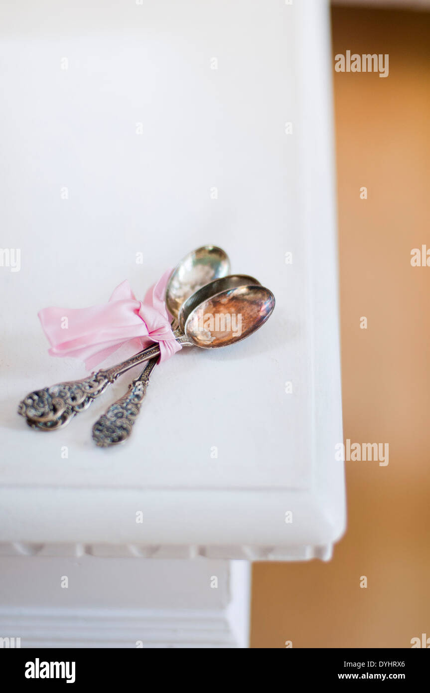Three Antique Silver Spoons with Pink Ribbon Lying on White Table Stock Photo