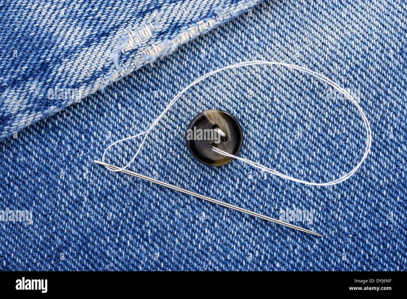 Sewing a button on blue jeans fabric Stock Photo Alamy
