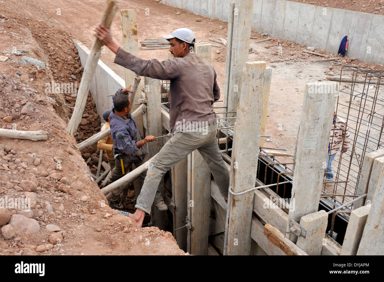 Construction workmen installing traditional timber formwork for concrete pour on new canal for water supply, Marrakech Morocco Stock Photo