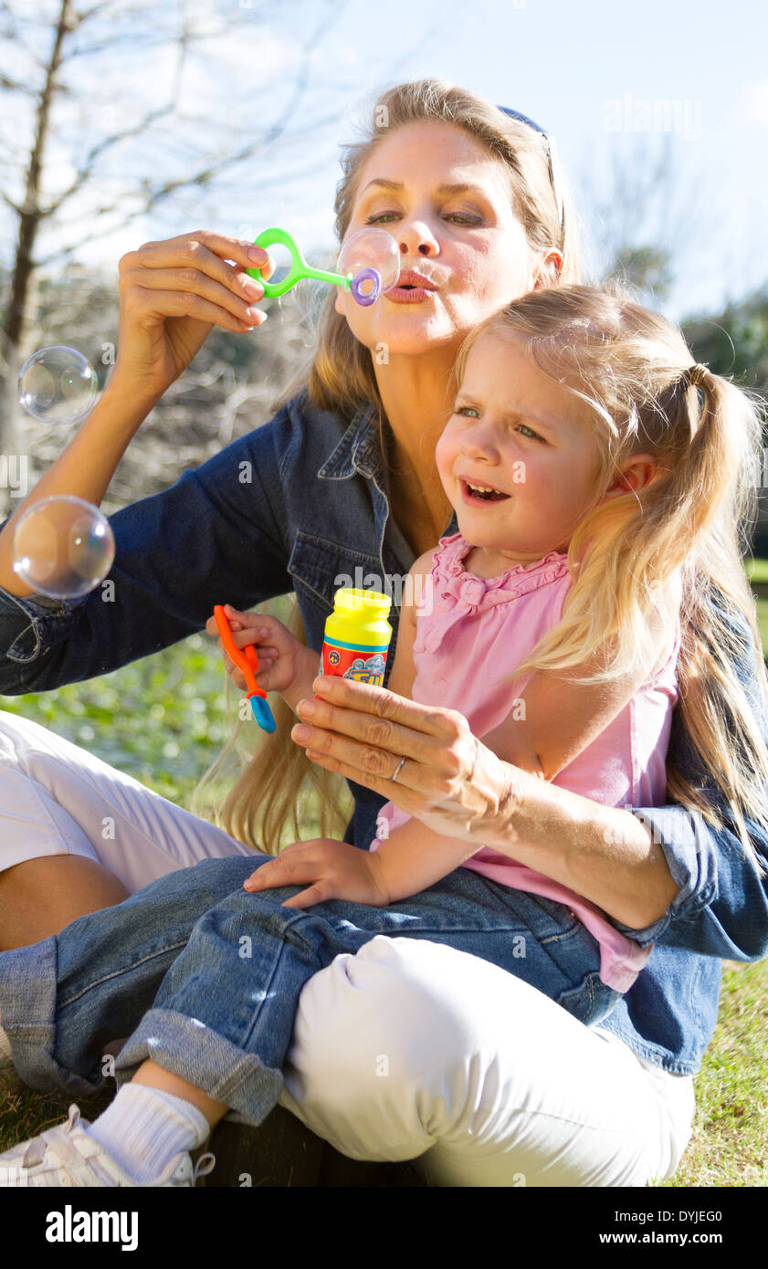 mother and daughter blowing bubbles in park Stock Photo