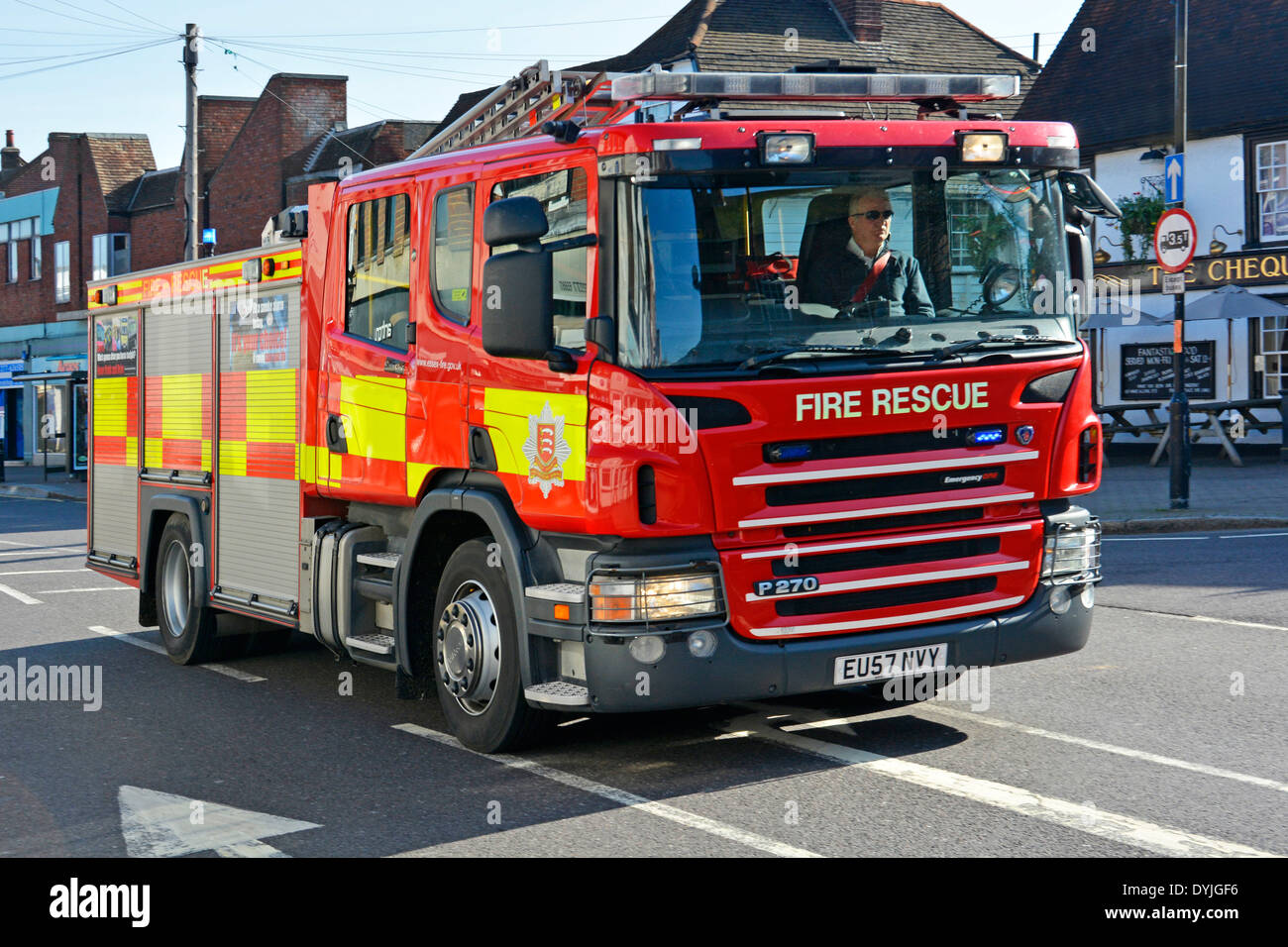 Essex Fire and Rescue lorry truck fire brigade engine appliance crew on emergency call driving along shopping high street Billericay Essex England UK Stock Photo