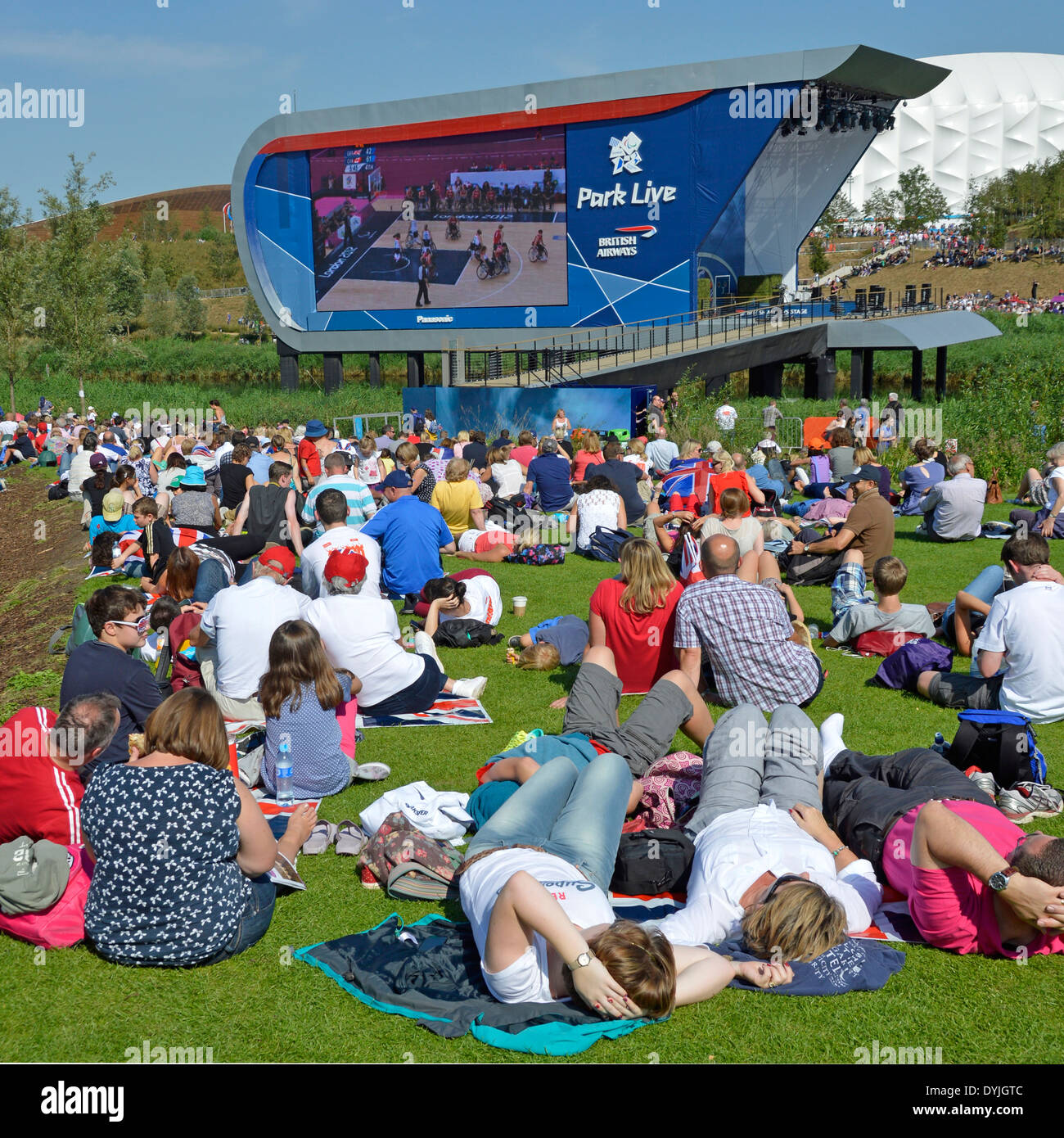 Big two sided TV screen in London 2012 Olympic Park with spectators relaxing watching Paralympic Games on a hot summers day Stock Photo