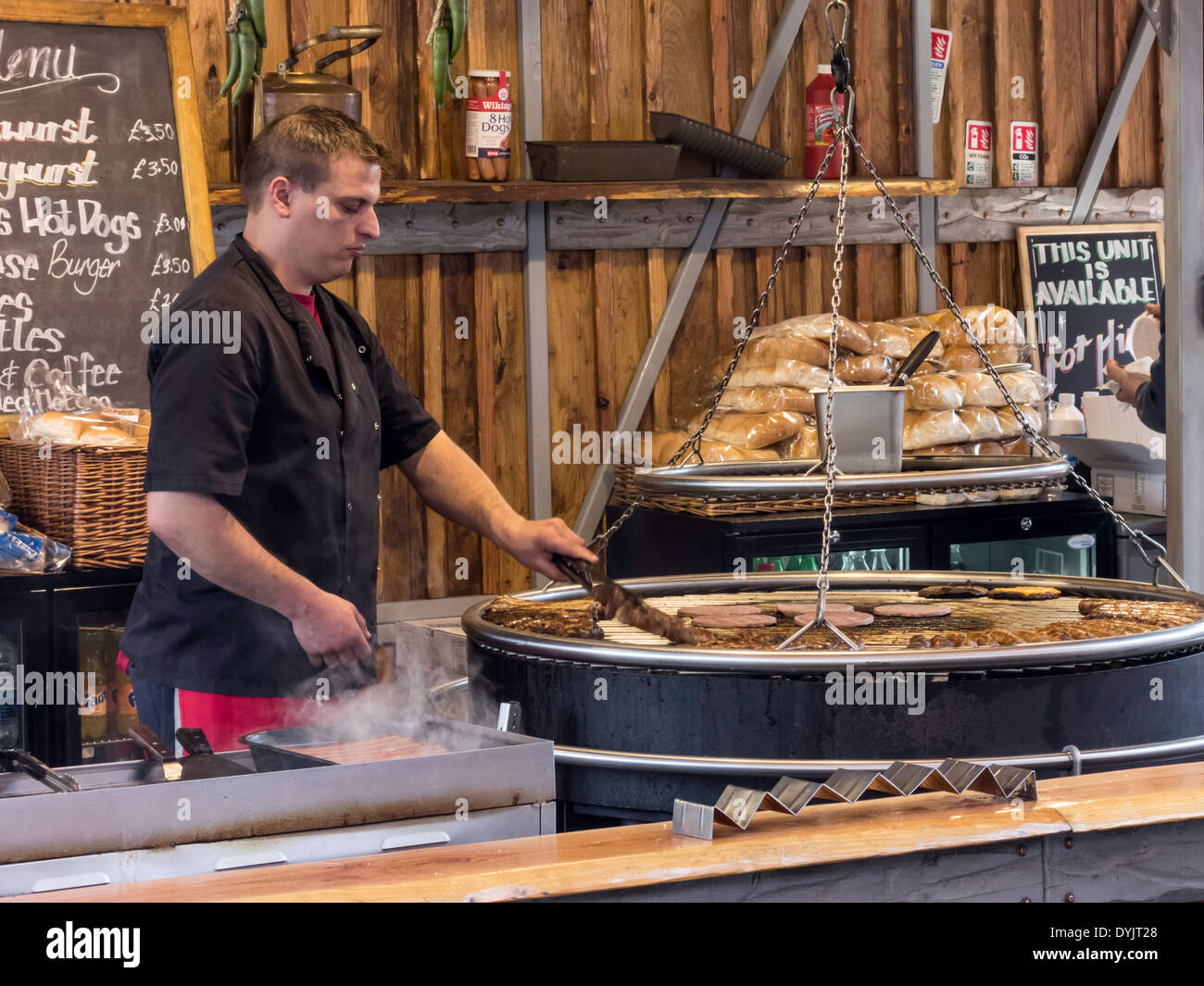 A man cooking burgers and sausages on a stall in a Euro street market