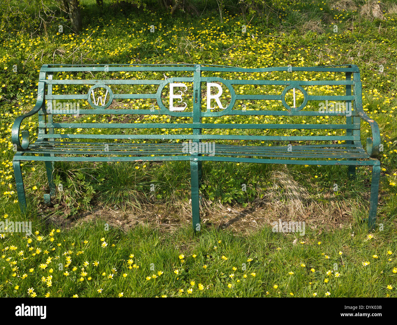 Green wrought iron bench with Women's Institute and Elizabeth Regina reference. On grassy background with lesser celandine Stock Photo